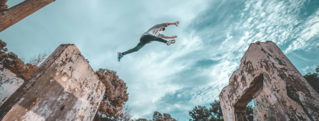 Photograph of a person leaping over the crumbling buildings of ruins
