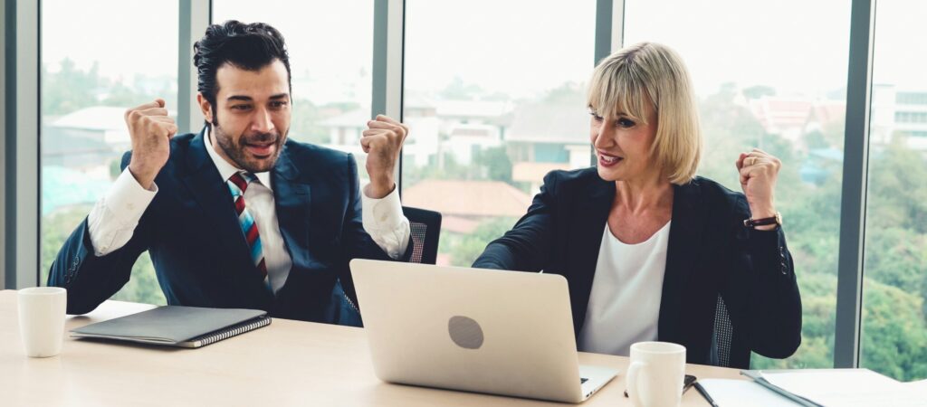 Photograph of two executives looking at a laptop and cheering.